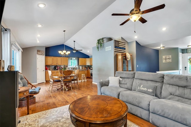 living room featuring ceiling fan with notable chandelier, light hardwood / wood-style floors, and vaulted ceiling