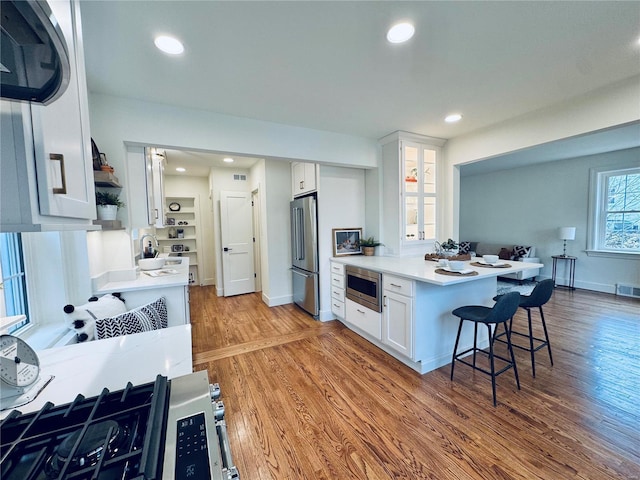 kitchen with light wood-style flooring, stainless steel appliances, white cabinetry, light countertops, and open shelves