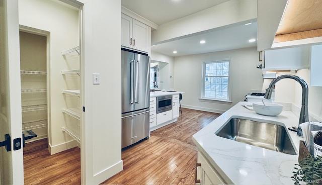 kitchen with light stone counters, wood finished floors, a sink, white cabinets, and appliances with stainless steel finishes