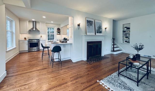 living room featuring built in shelves, a fireplace with flush hearth, dark wood finished floors, and baseboards