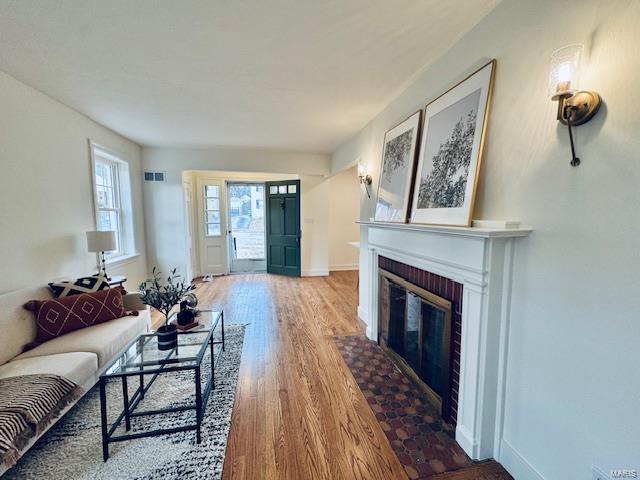 living room featuring visible vents, a fireplace, baseboards, and wood finished floors