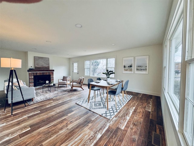 dining area featuring dark wood-style flooring, a brick fireplace, visible vents, and baseboards