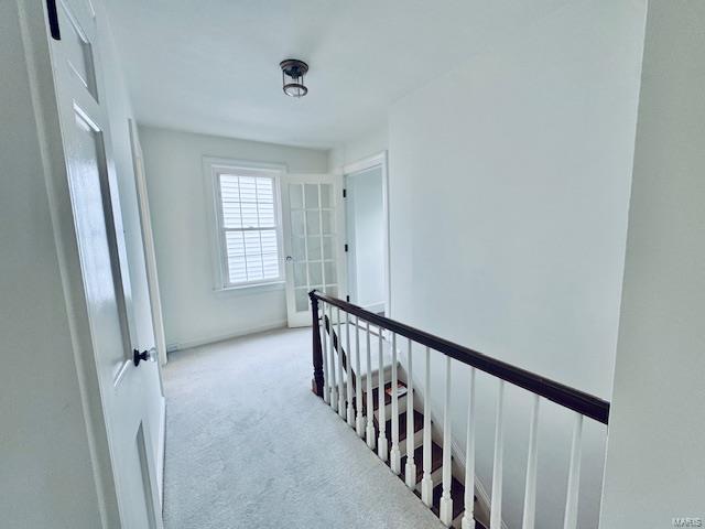 hallway with light carpet and an upstairs landing