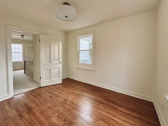 unfurnished bedroom featuring multiple windows, wood finished floors, and baseboards