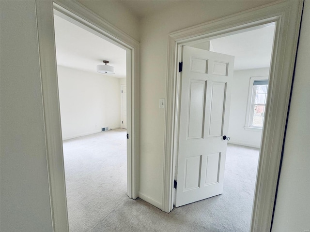 hallway featuring baseboards, visible vents, and light colored carpet