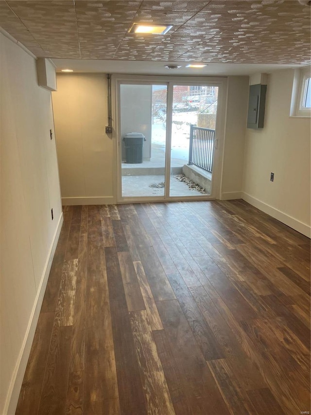 empty room with electric panel, baseboards, and dark wood-type flooring