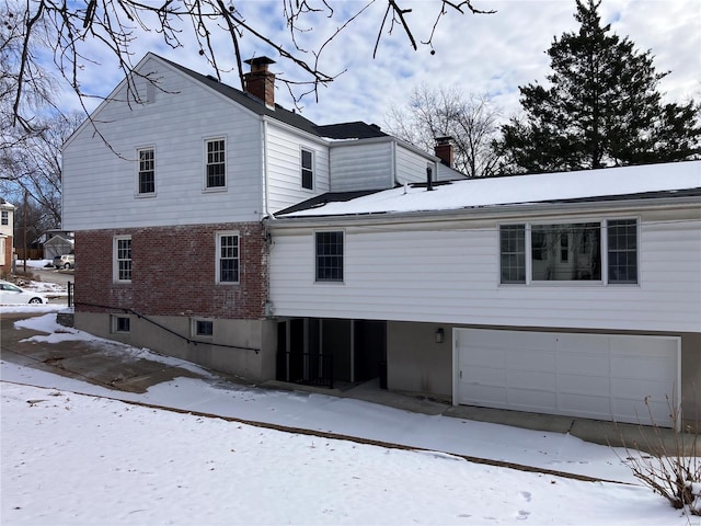 view of snowy exterior with a garage, brick siding, and a chimney