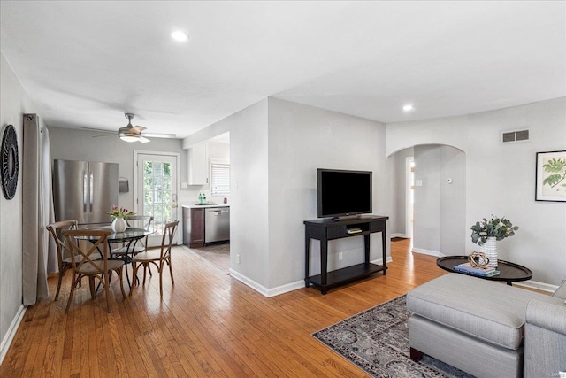 living area featuring arched walkways, visible vents, light wood-style flooring, and baseboards