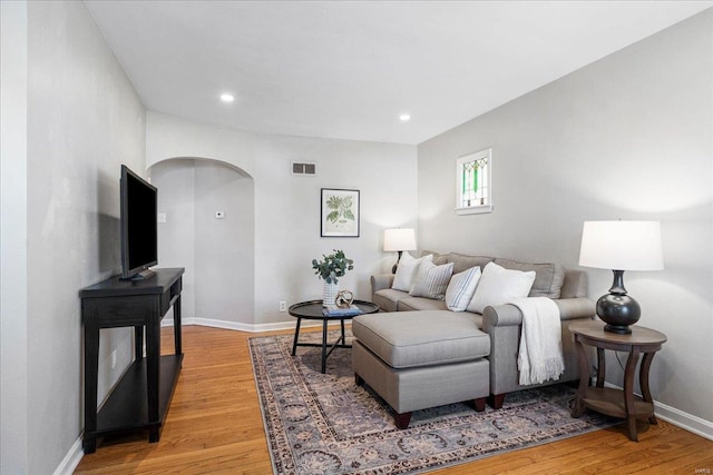 living room with light wood-type flooring, visible vents, recessed lighting, arched walkways, and baseboards