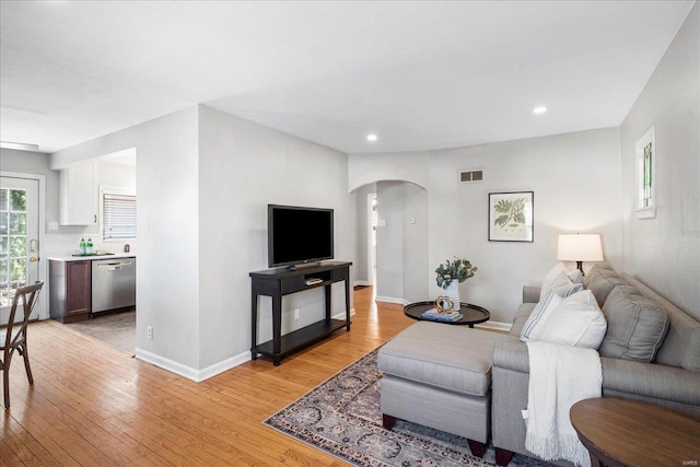 living area with visible vents, arched walkways, baseboards, and light wood finished floors