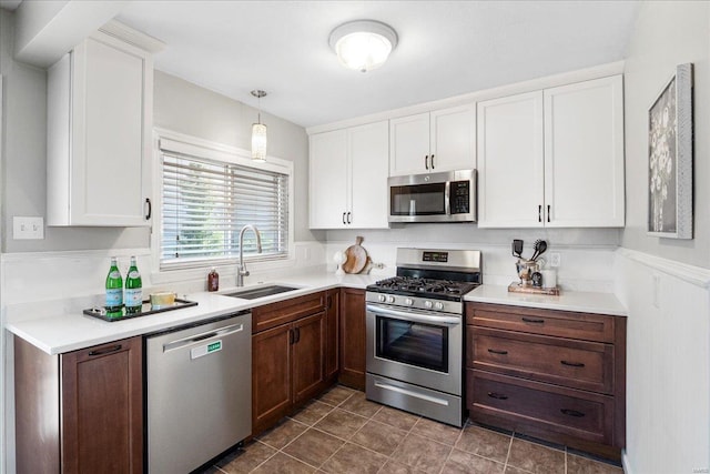 kitchen featuring a sink, light countertops, appliances with stainless steel finishes, white cabinetry, and dark tile patterned flooring