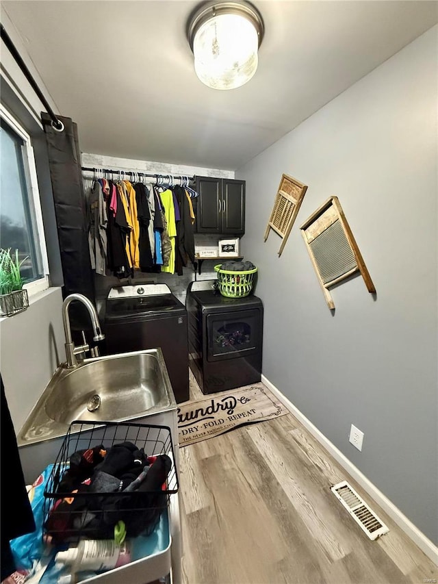 washroom featuring sink, cabinets, washing machine and dryer, and light hardwood / wood-style floors