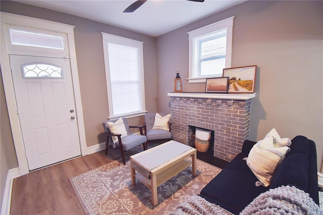 foyer entrance with a brick fireplace, ceiling fan, baseboards, and wood finished floors