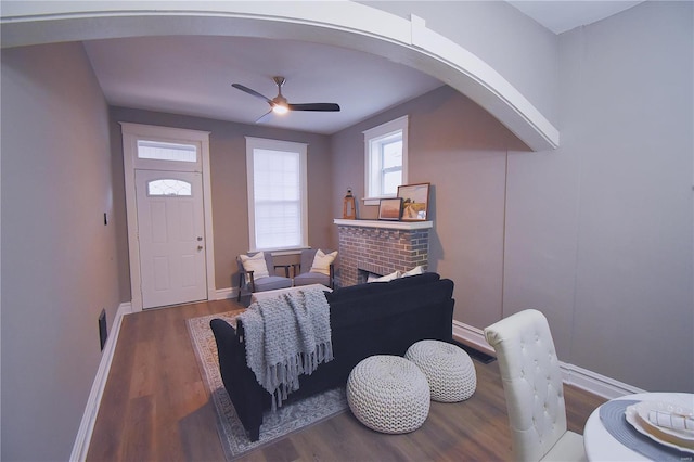 interior space with arched walkways, a fireplace, wood finished floors, and a ceiling fan