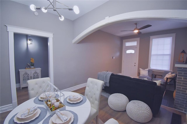 dining area featuring baseboards, arched walkways, dark wood finished floors, and ceiling fan with notable chandelier