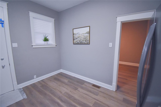 spare room with wood finished floors, visible vents, and baseboards