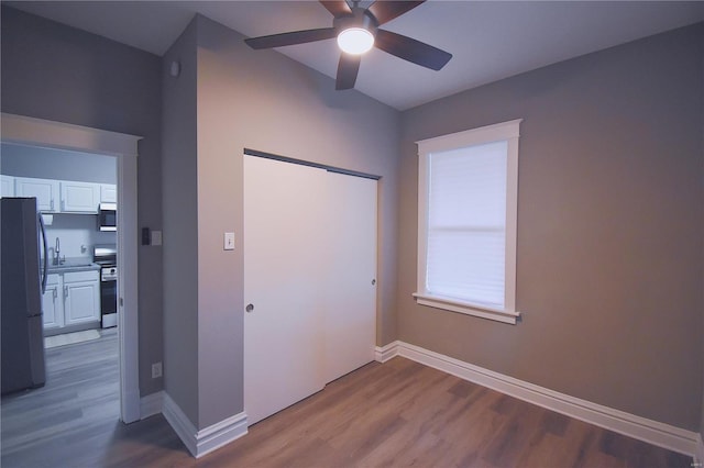 unfurnished bedroom with a closet, baseboards, wood finished floors, and freestanding refrigerator