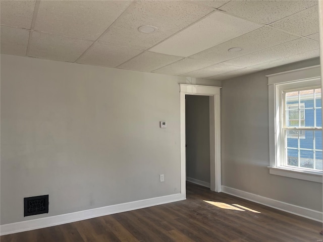 unfurnished room with a drop ceiling, visible vents, baseboards, and dark wood finished floors