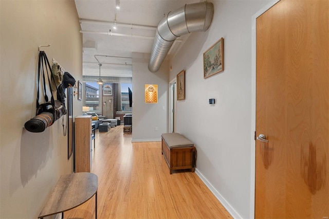 hall featuring light wood-style floors, baseboards, and track lighting