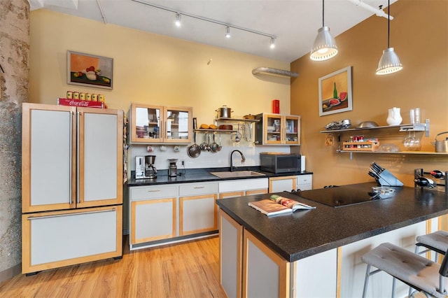 kitchen with dark countertops, glass insert cabinets, a breakfast bar area, open shelves, and a sink