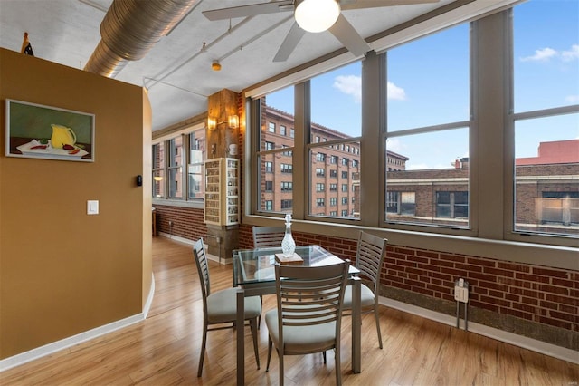 dining space featuring light wood finished floors, brick wall, baseboards, and ceiling fan