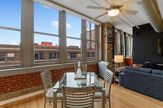 dining area with ceiling fan, brick wall, and light wood-style floors