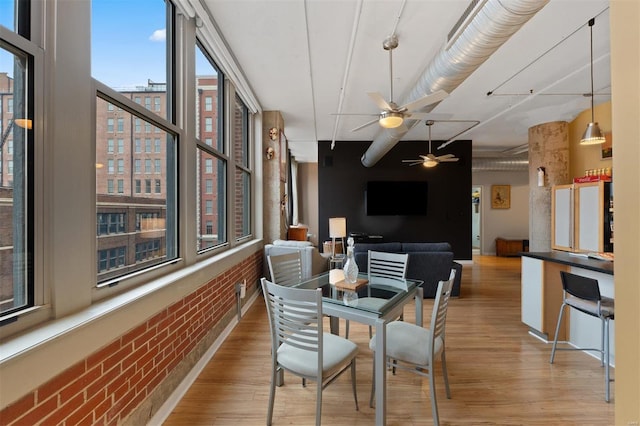 dining room featuring ceiling fan, brick wall, and light wood-style floors