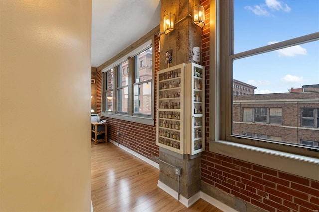 hallway with a healthy amount of sunlight, brick wall, baseboards, and wood finished floors