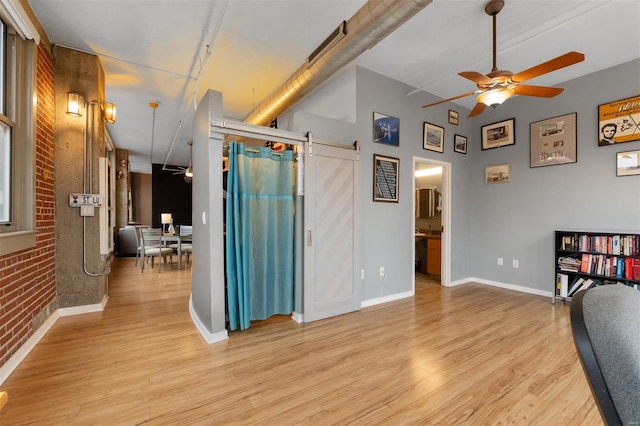 hallway featuring brick wall, a barn door, light wood-type flooring, and baseboards