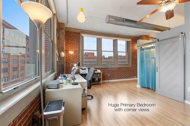 office area with a city view, a barn door, light wood-style floors, ceiling fan, and brick wall