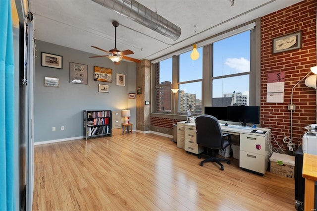 office space with light wood-type flooring, baseboards, and brick wall