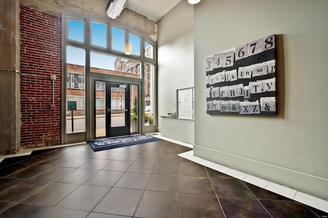 foyer entrance with brick wall, dark tile patterned floors, a towering ceiling, and baseboards