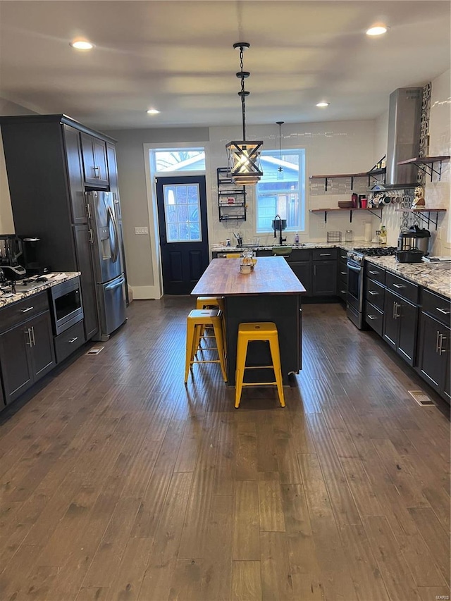 kitchen featuring light stone counters, dark wood-style flooring, open shelves, stainless steel appliances, and a kitchen island