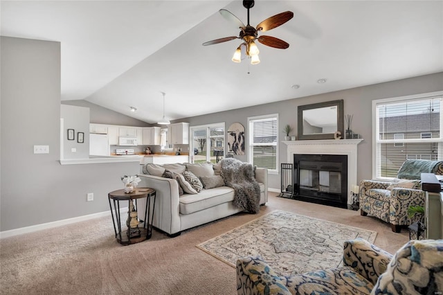 living area featuring baseboards, lofted ceiling, a fireplace with flush hearth, ceiling fan, and light colored carpet