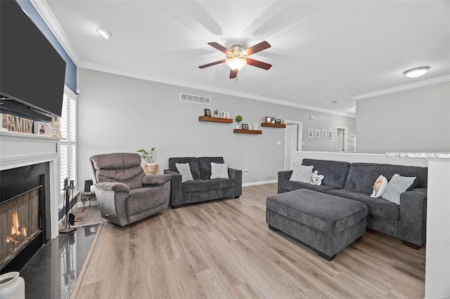 living area with crown molding, visible vents, ceiling fan, wood finished floors, and a lit fireplace