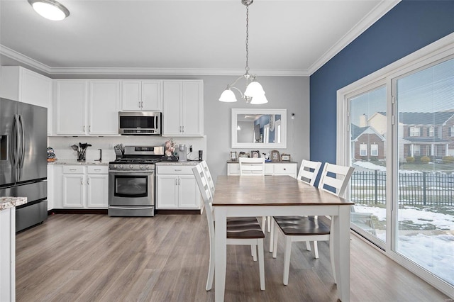 kitchen with white cabinets, appliances with stainless steel finishes, light stone counters, decorative light fixtures, and crown molding