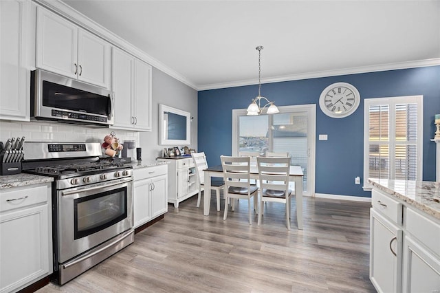 kitchen featuring white cabinets, stainless steel appliances, crown molding, and decorative light fixtures