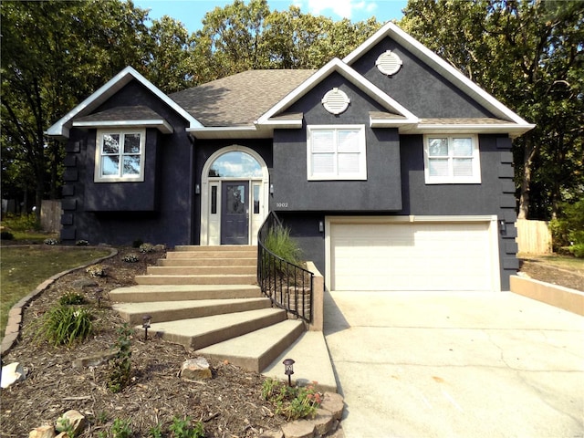 raised ranch featuring driveway, an attached garage, roof with shingles, and stucco siding