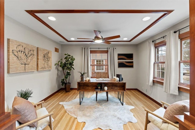 office area featuring a raised ceiling, light wood-type flooring, and ceiling fan