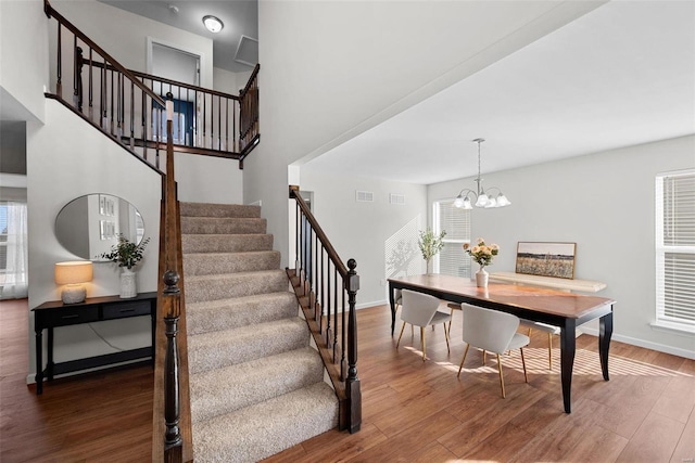 staircase featuring wood finished floors, visible vents, a towering ceiling, baseboards, and an inviting chandelier