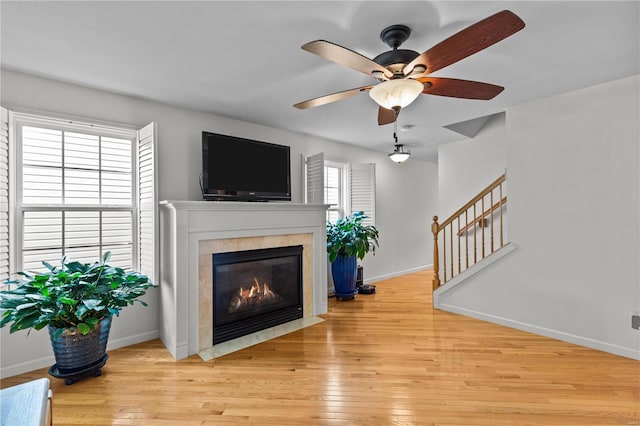 living room with ceiling fan, a high end fireplace, and light hardwood / wood-style flooring