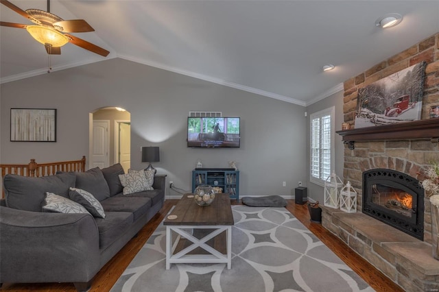 living room featuring hardwood / wood-style flooring, lofted ceiling, a stone fireplace, ornamental molding, and ceiling fan