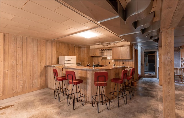 kitchen with a kitchen breakfast bar, unfinished concrete flooring, wood walls, and light countertops