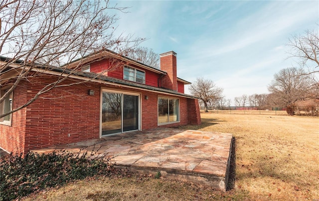 back of house featuring a yard, brick siding, a chimney, and a patio area