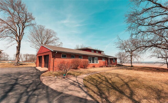 exterior space with aphalt driveway, an attached garage, a lawn, and brick siding