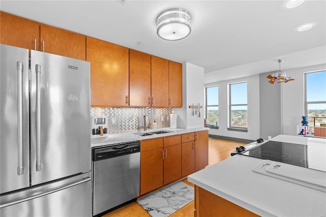 kitchen featuring hanging light fixtures, stainless steel appliances, light hardwood / wood-style flooring, sink, and backsplash