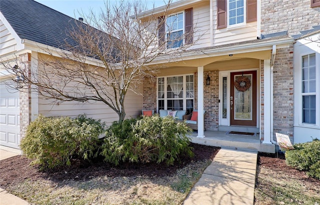 doorway to property featuring covered porch, brick siding, and an attached garage