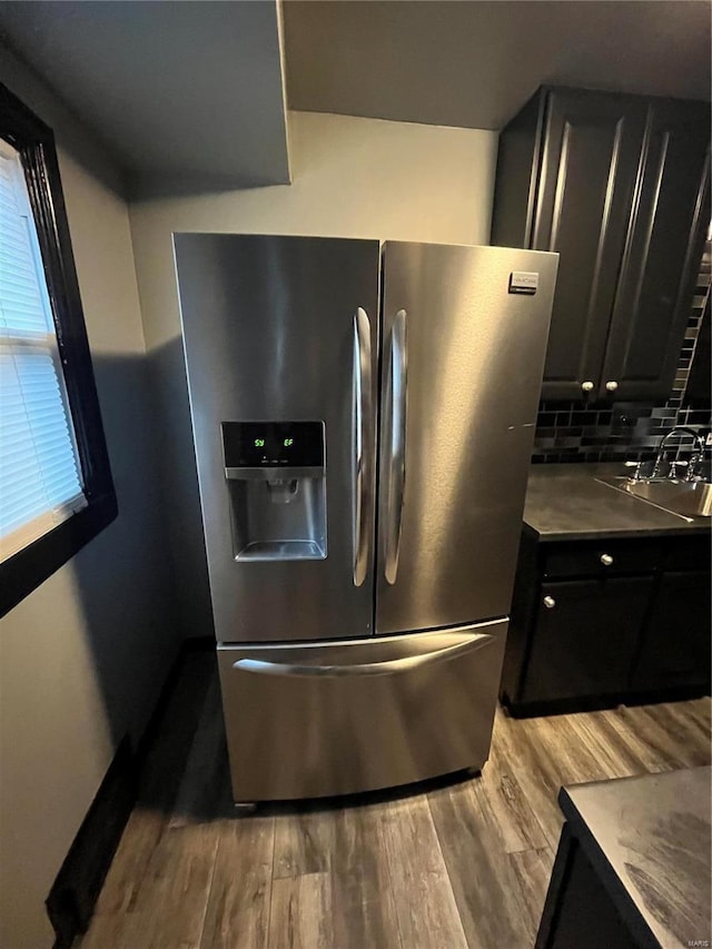 kitchen featuring decorative backsplash, stainless steel fridge with ice dispenser, dark countertops, light wood-type flooring, and a sink