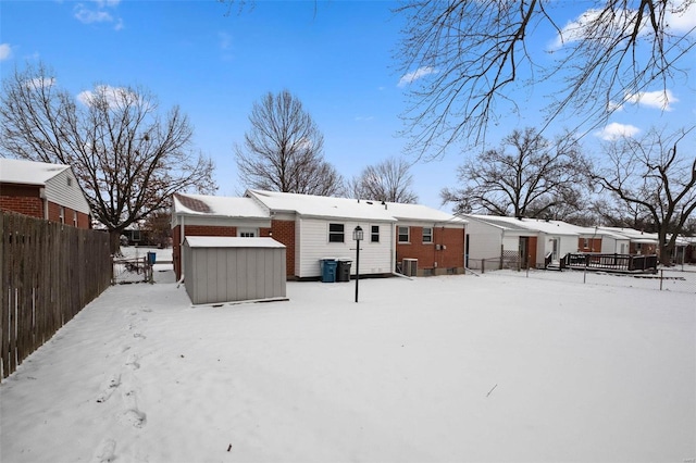 snow covered house with a shed, central AC, fence, and an outbuilding