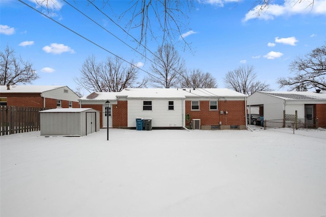 snow covered back of property featuring central AC unit, an outbuilding, fence, a shed, and brick siding